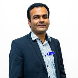 Practice Manager headshot, wearing black blazer, white and blue pinstripe shirt and purple name badge, with white background.