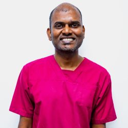 Headshot of Dr wearing pink scrubs with white wall background